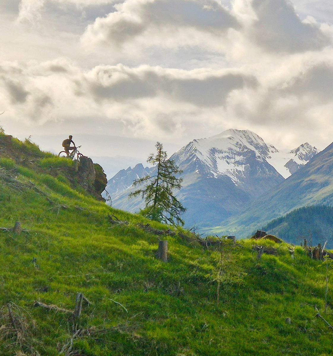 Mountainbiker genießt auf einem Felsvorsprung das Panorama im Virgental - Hotel Ortnerhof