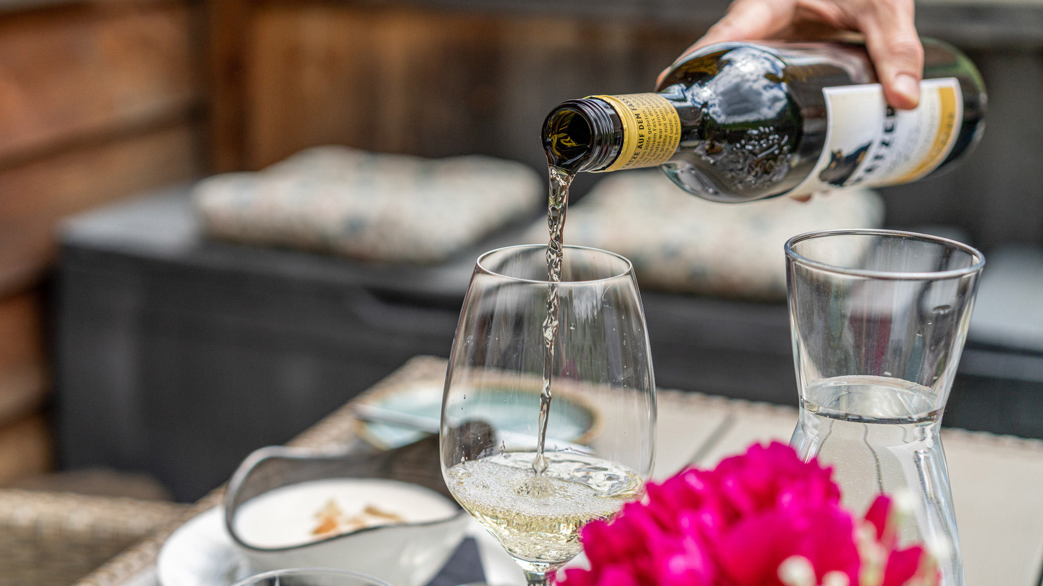 Ein gedeckter Tisch auf der Terrasse und Weißwein wird in ein Glas eingeschenkt - Hotel Ortnerhof