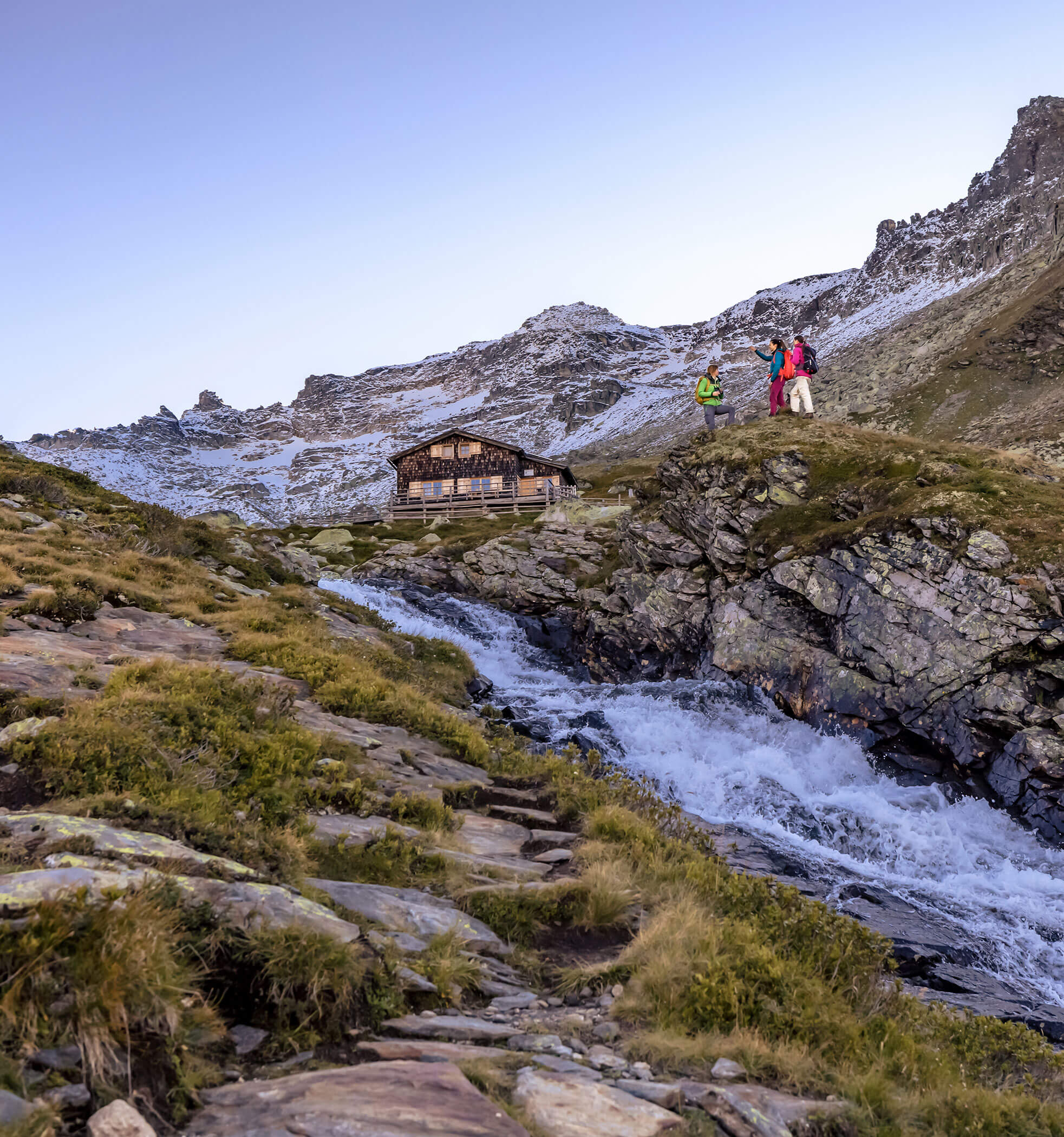 Drei Wanderer über einem Bach mit Almhütte im Hintergrund - Hotel Ortnerhof