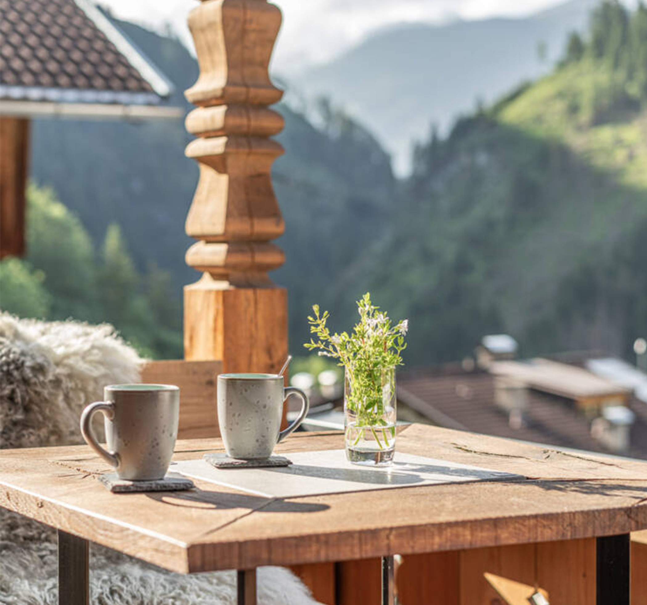 Wooden table on the balcony with two cups and a glass with flowers in it - Hotel Ortnerhof