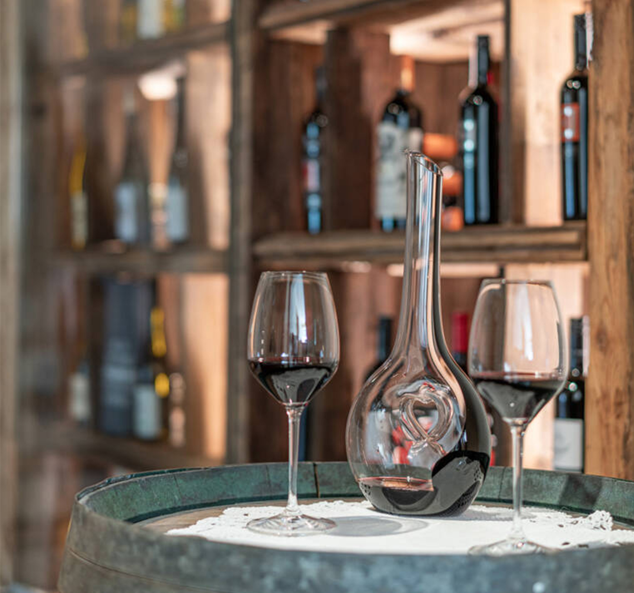 A carafe of red wine and two glasses, with a wine rack behind them - Hotel Ortnerhof